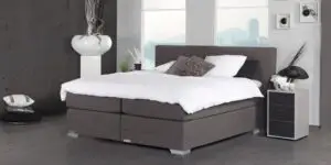 Boxspring Caresse 9350 in slaapkameropstelling met gestoffeerd hoofdbord, tweepersoonsmatras en neutrale beddengoedkleuren.