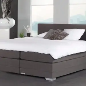 Boxspring Caresse 9350 in slaapkameropstelling met gestoffeerd hoofdbord, tweepersoonsmatras en neutrale beddengoedkleuren.