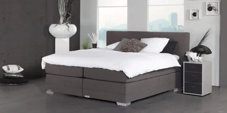 Boxspring Caresse 9350 in slaapkameropstelling met gestoffeerd hoofdbord, tweepersoonsmatras en neutrale beddengoedkleuren.